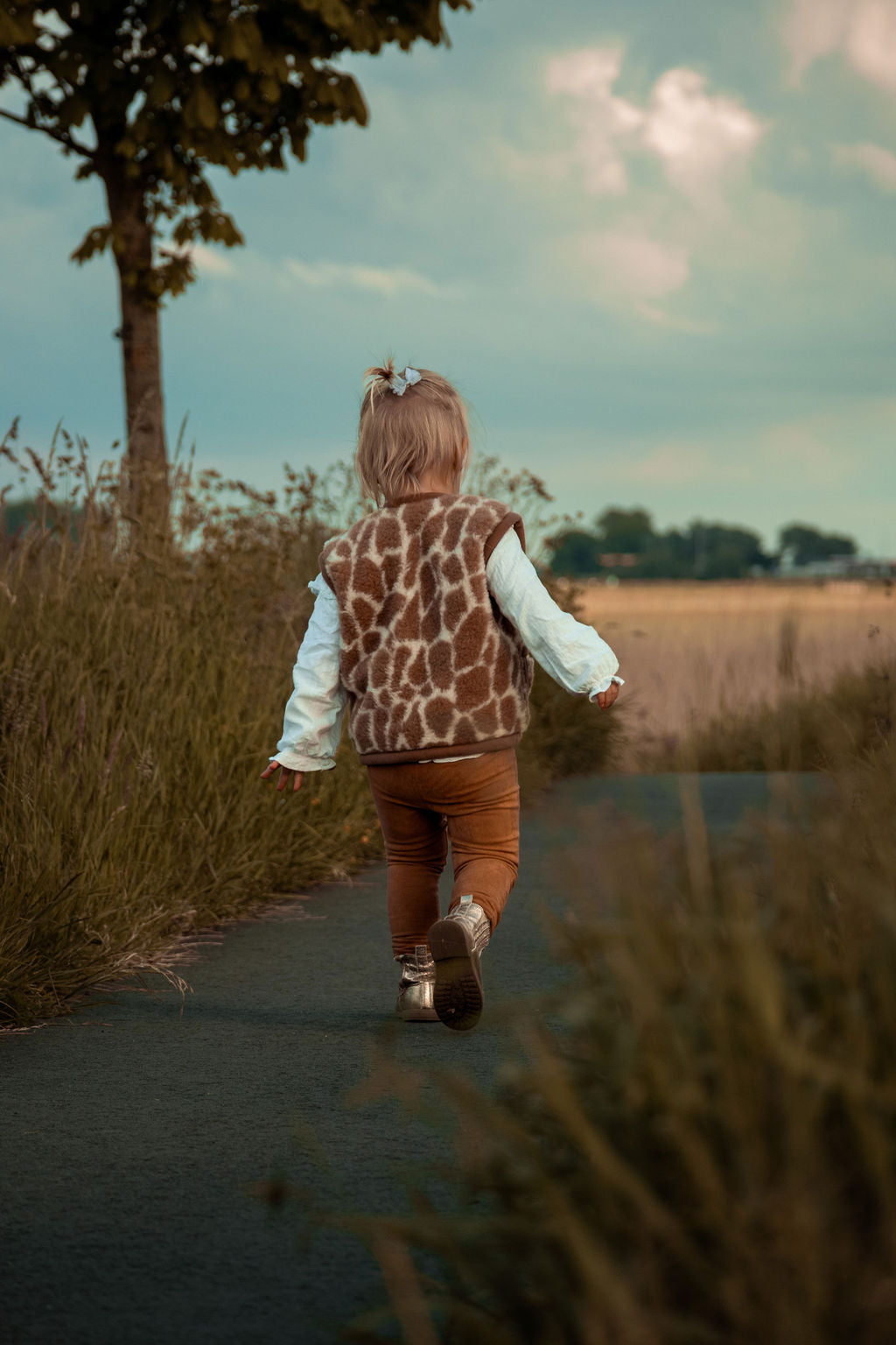Peuter in wollen giraffeprint-bodywarmer, gezien van achteren op een pad