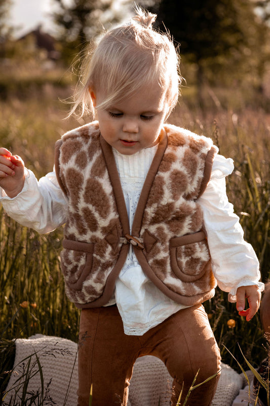 Peuter in wollen bodywarmer met giraffeprint loopt door hoog gras
